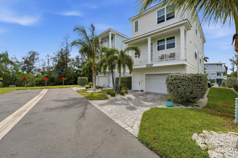 Welcoming curb appeal with manicured tropical landscaping, a paver driveway, and an oversized two-car garage on this beautifully appointed coastal home.