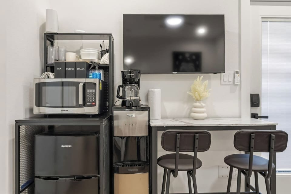 The room features a kitchenette with a mini refrigerator, a TV, and a dining area for two guests.