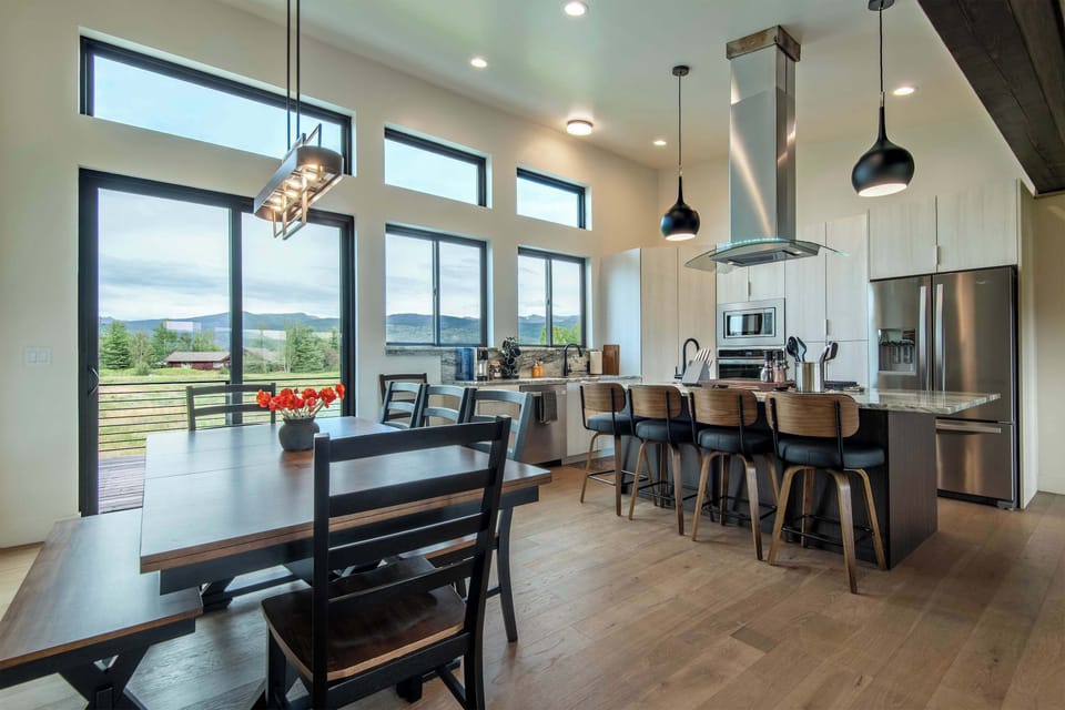 Sun-drenched open-concept kitchen flows into dining and a music corner — pendant lights, bar seating, and mountain views make every meal feel like an occasion.