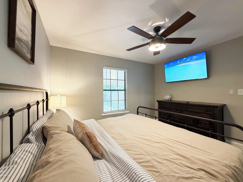 Cozy bedroom with TV, ceiling fan, and calming neutral decor