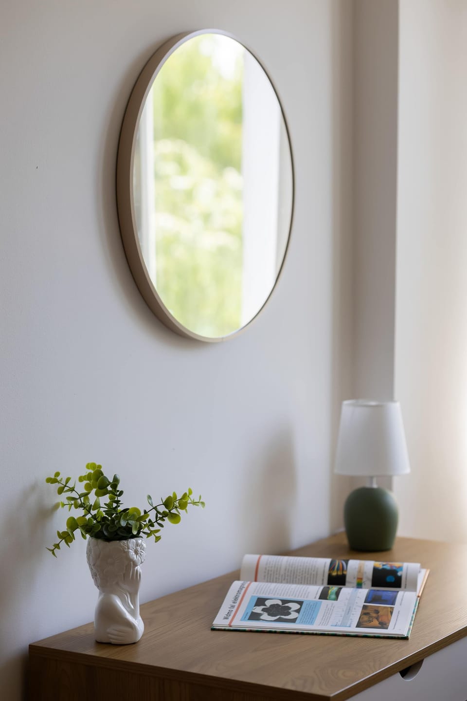 A small wooden table with a plant and decorative accessories. A round mirror adds a stylish touch to the space.