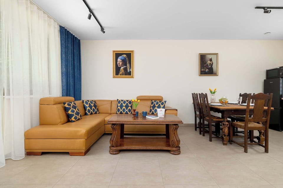 The expansive open-plan lounge combines a tan leather corner sofa, a rustic wooden coffee table, and a formal dining area. Minimalist track lighting on the ceiling ensures the entire space remains bright and welcoming.