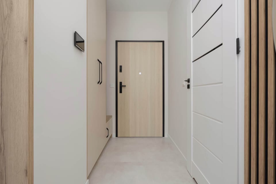An entryway perspective looks directly toward the main apartment door, which is framed by light wood panels. The clean, bright floors make the entry point feel spacious and inviting.