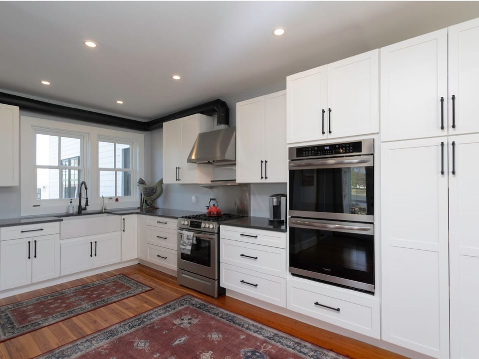 Picture yourself cooking with friends in this bright, modern kitchen featuring double ovens, gas range, and sleek white cabinetry with warm wood floors underfoot.