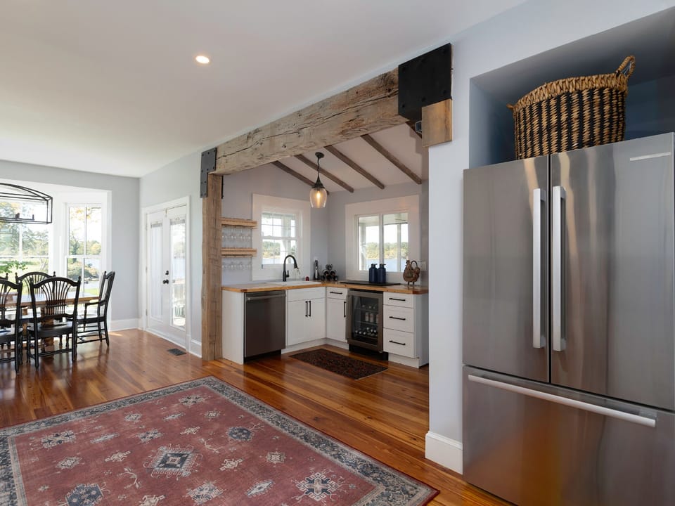 Gather in this inviting open kitchen with rustic beams and modern appliances. Imagine preparing meals with natural light streaming through multiple windows, while staying connected to your dining area.