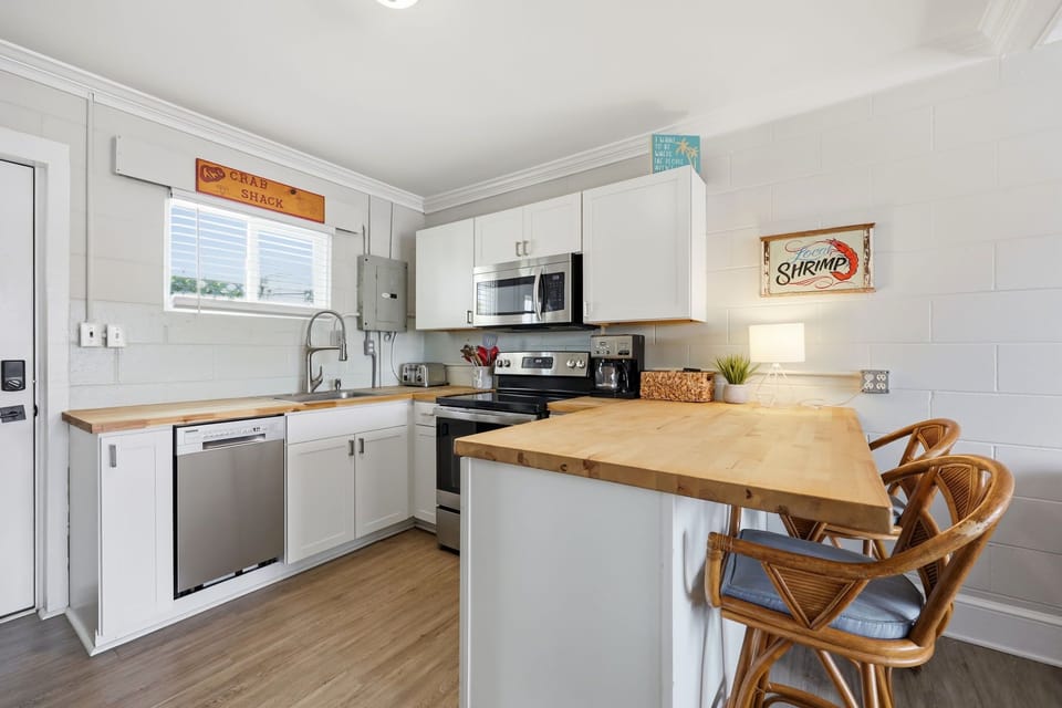Your fully equipped kitchen features warm wood countertops, modern appliances, and a cozy breakfast bar with rattan stools—perfect for preparing meals and sharing stories over morning coffee.