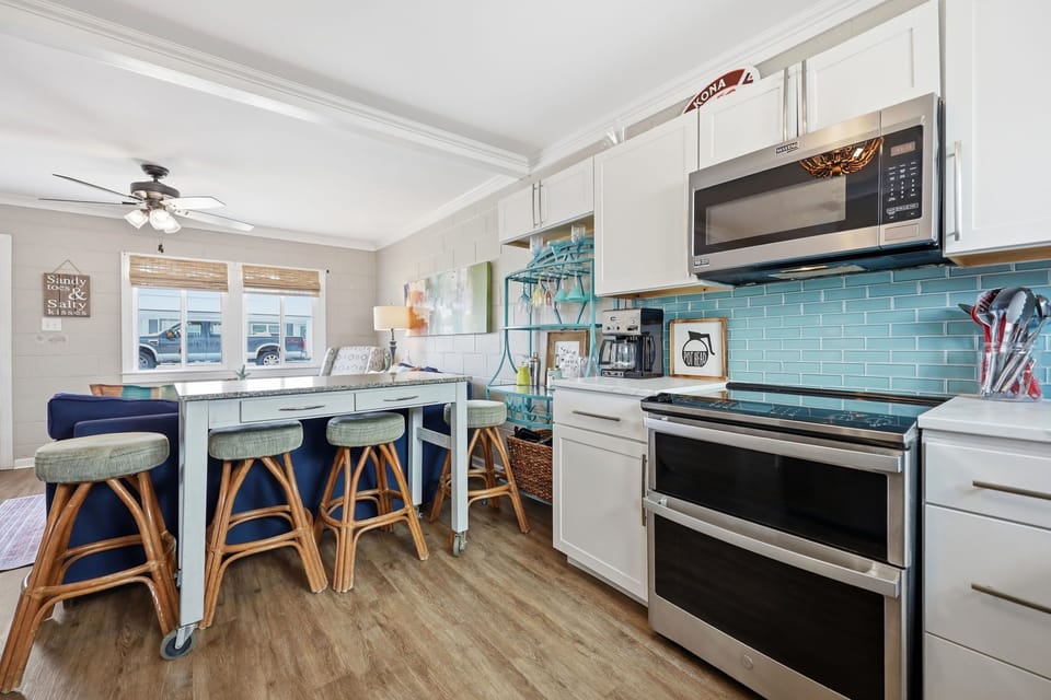 Picture yourself cooking in this bright coastal kitchen, complete with turquoise tile backsplash, stainless appliances, and a charming island where you can gather for meals and morning coffee together.
