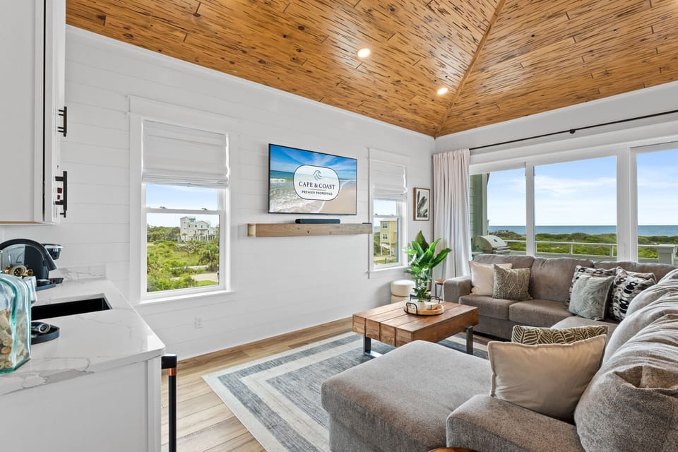 Relax in your sunlit living space with stunning ocean views, vaulted wood ceilings, and cozy seating perfect for unwinding after a beach day.
