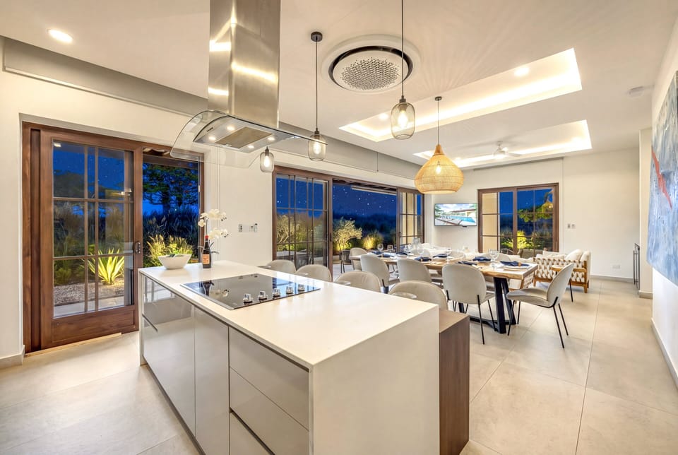 A sleek kitchen island and pendant-lit dining table set the scene for an elegant evening in. The tropical garden glows just beyond the glass.