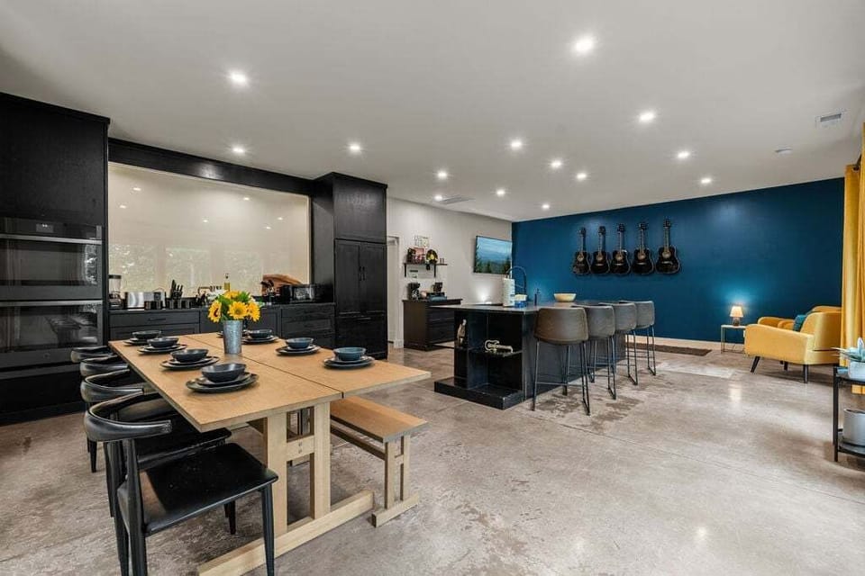 Spacious open kitchen and dining area with long table, island seating, black cabinetry, and bold blue accent wall.