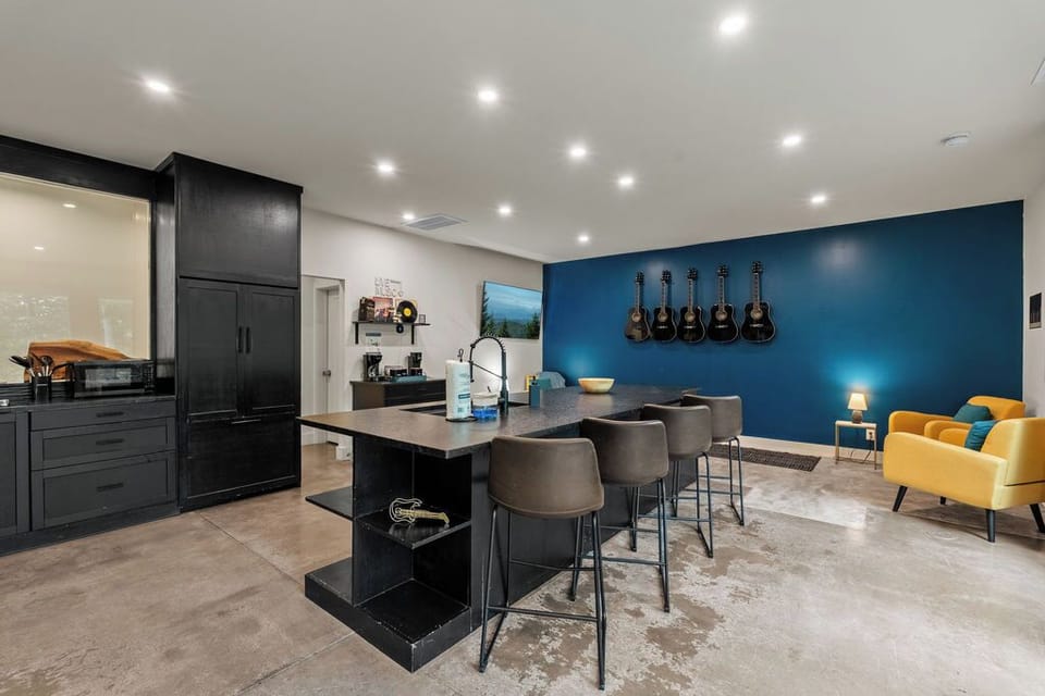 Modern kitchen island with bar seating, black cabinets, and a cozy sitting area with music-themed wall decor.