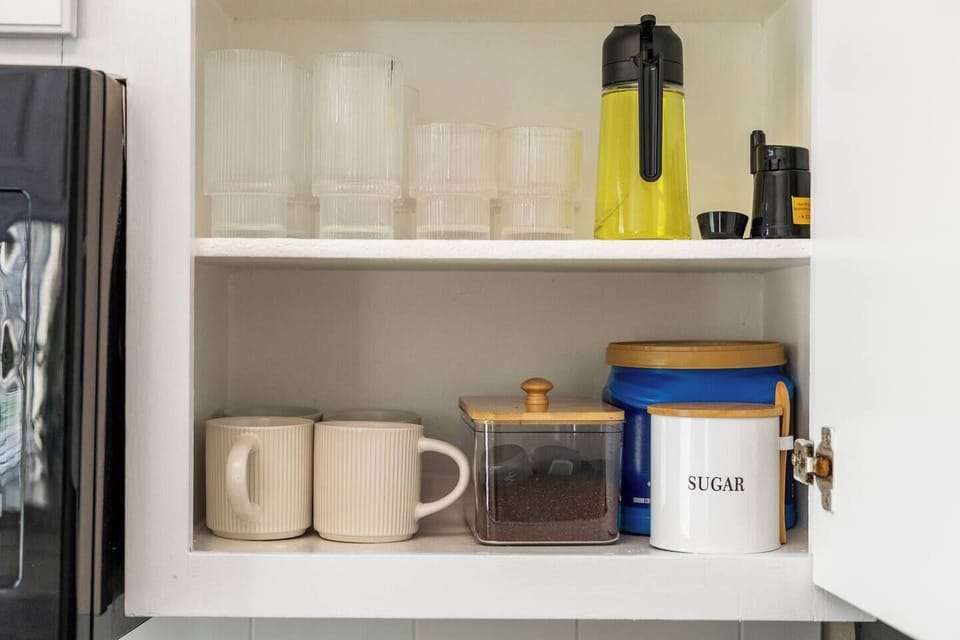 Kitchen shelf with mugs, drinking glasses, coffee supplies, sugar, and a coffee maker, providing convenient essentials for preparing morning drinks during your stay.