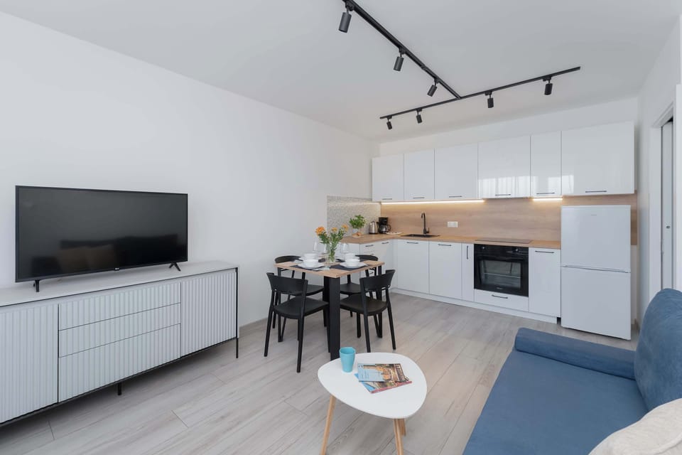 A wide view of the living room features a flat-screen television placed atop a long white sideboard. The adjacent dining table is neatly set for a meal, showcasing the apartment's readiness for guests.