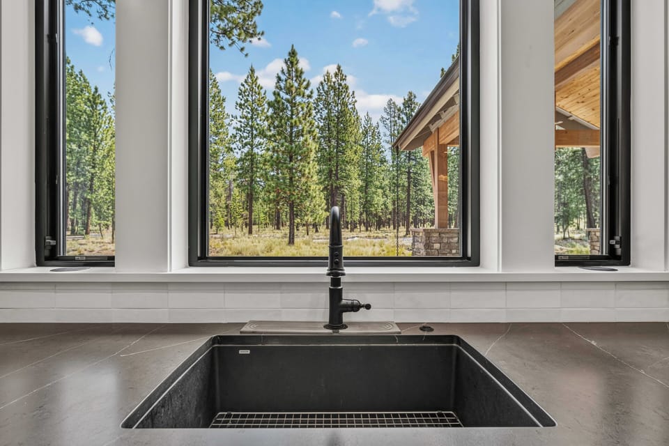 Picture yourself prepping meals with this inspiring view: towering pines and open meadows framed by sleek windows above a modern farmhouse sink, bringing the serenity of nature right into your kitchen.
