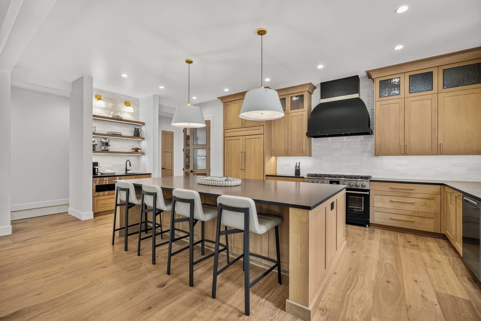A spacious modern kitchen featuring natural wood cabinetry, sleek pendant lighting, and an inviting island with seating—perfect for preparing meals and gathering with loved ones.