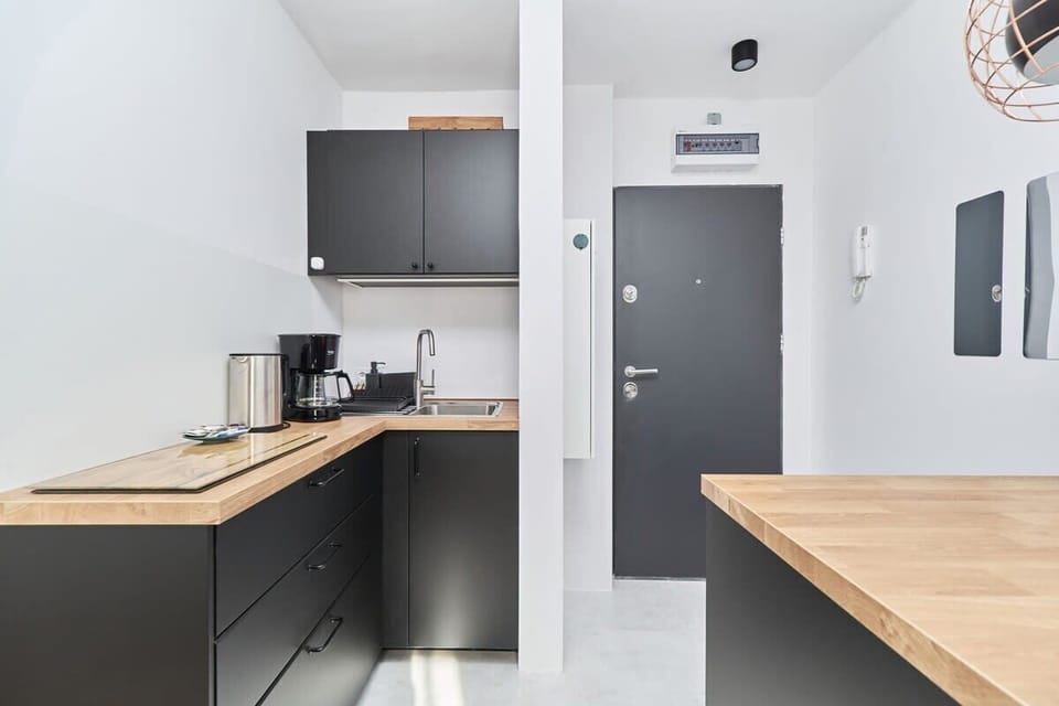 A modern kitchenette with sleek black cabinets, a wooden countertop, and appliances, including a coffee maker and kettle.