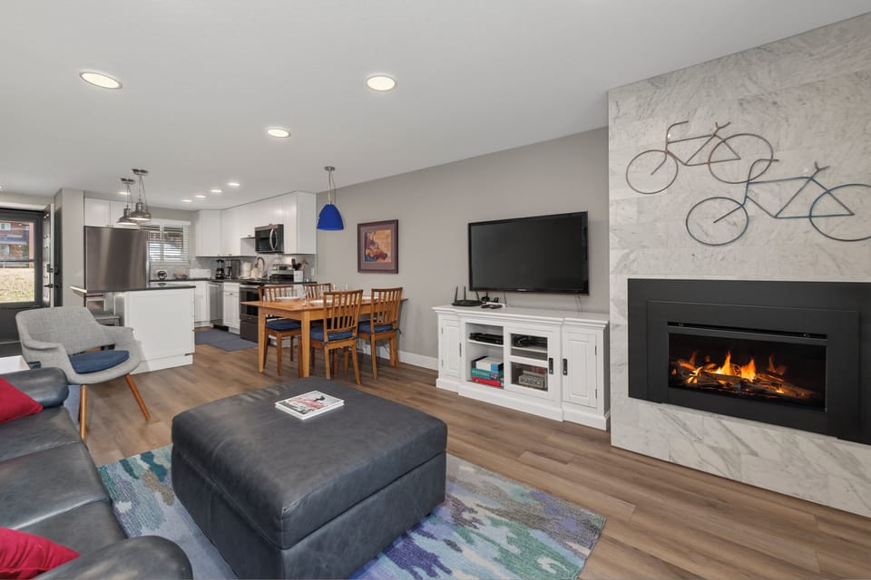 Unwind in this stylish open-concept living space featuring a cozy fireplace, modern kitchen, and inviting dining area—perfect for relaxing after your adventures.