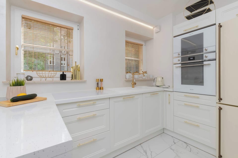 A luxurious white kitchen features glossy cabinetry, integrated appliances, and marble-inspired finishes. The clean design provides both style and practicality.
