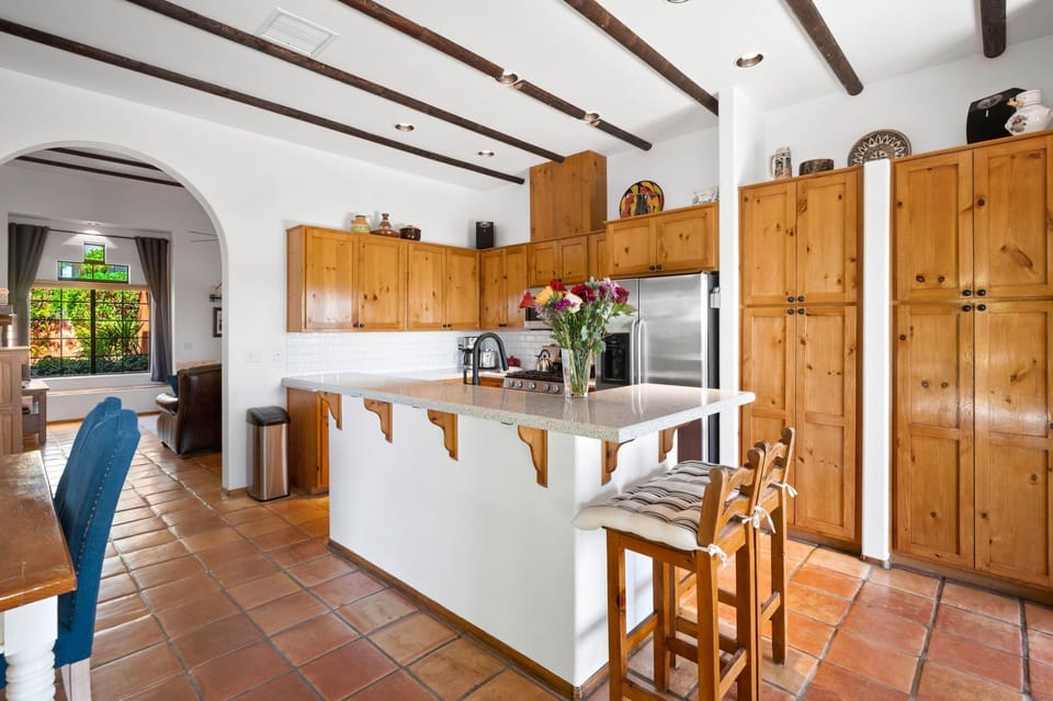 Gather around the spacious kitchen island under rustic wood-beamed ceilings. Enjoy abundant storage, stainless appliances, and natural light streaming through arched windows as you prepare meals together.