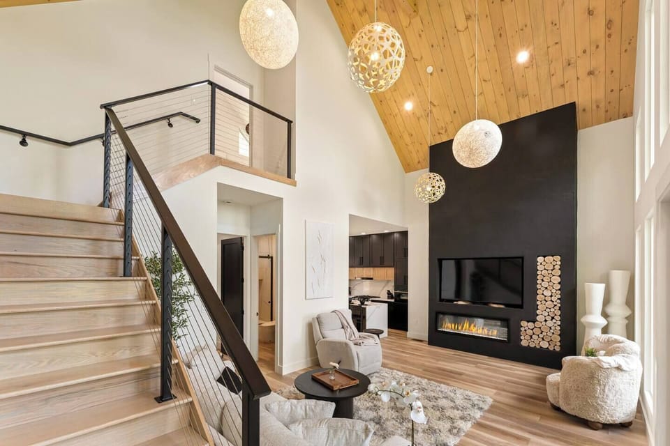 Relax in the grand living room featuring soaring cathedral ceilings, large windows, and a cozy fireplace. Perfect for gathering, unwinding, or simply taking in the stunning views in style and comfort.