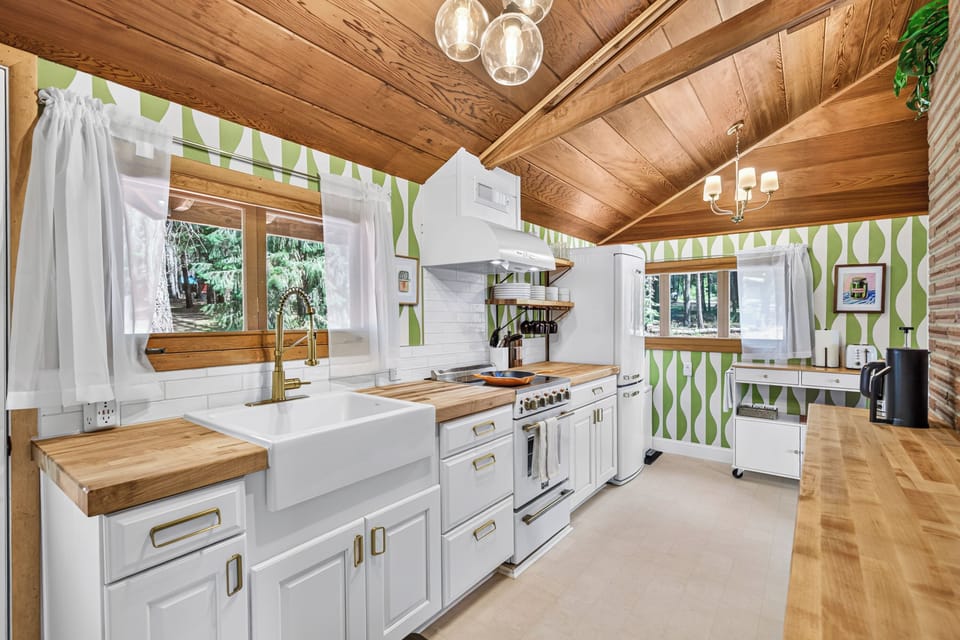 Bright cabin kitchen with wood ceilings, farmhouse sink, and forest views