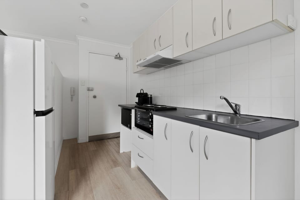 Modern compact kitchenette with cooktop, full-size fridge and coffee maker.