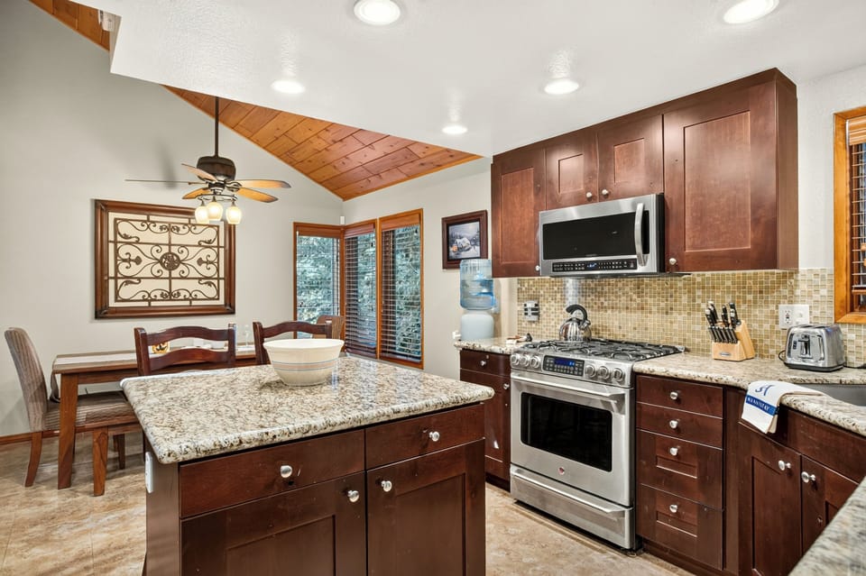 Warm kitchen with granite counters, stainless steel appliances, and a dining nook beneath vaulted wood ceilings.