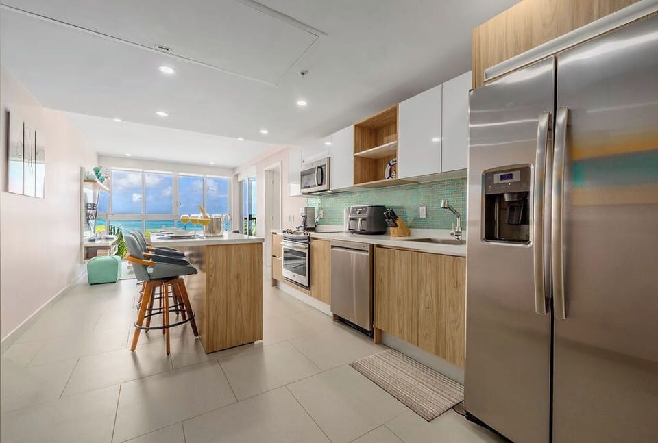 Picture yourself cooking in this fully equipped kitchen while gazing out at the stunning turquoise ocean through expansive windows. Modern appliances and stylish wood finishes make meal prep a breeze.