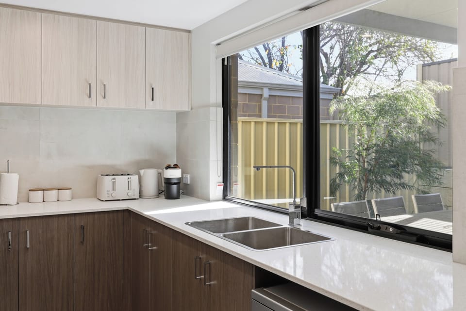 Enjoy a beautifully styled, light-filled kitchen space featuring high-quality appliances, a Nespresso coffee station, plenty of counter space, and an expansive window looking out to the patio.