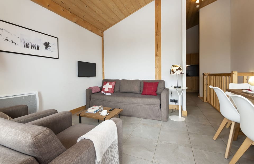 The living room's sloped wooden ceiling, mounted TV, and large windows bring the Alpine atmosphere inside.