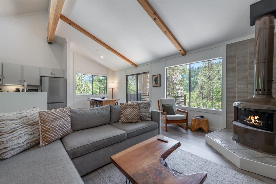 Relax in your bright, airy living space with soaring ceilings, exposed beams, and a cozy fireplace. Unwind on the plush sofa surrounded by forest views.