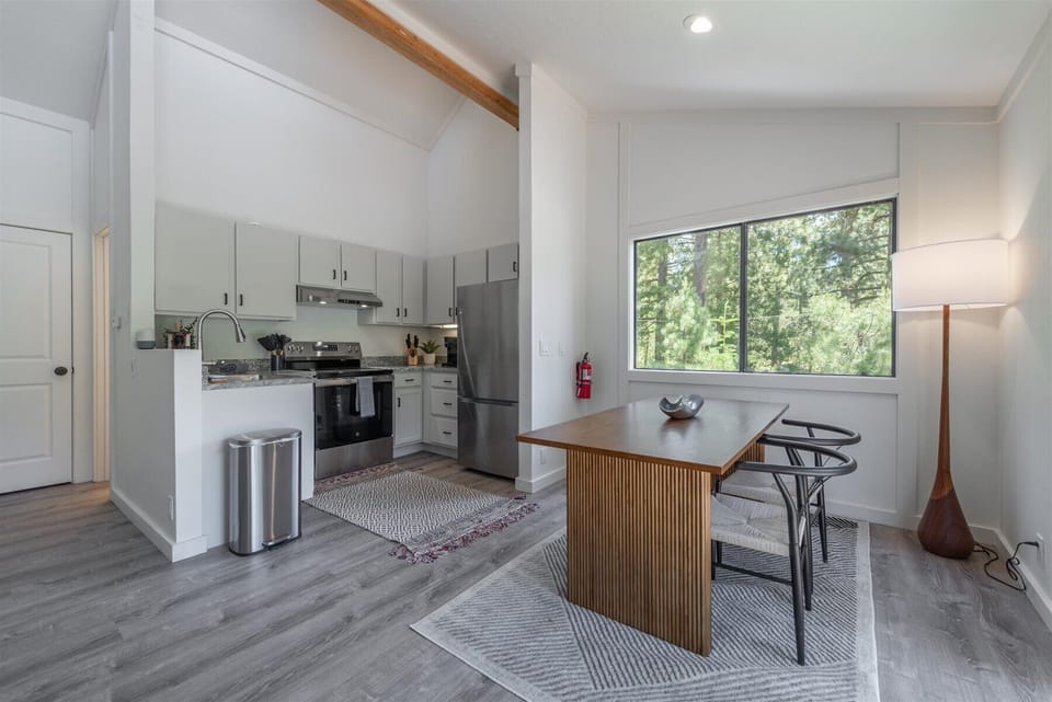 Your bright, modern kitchen features sleek appliances, warm wood accents, and abundant natural light—perfect for preparing meals while enjoying peaceful tree-lined views through the large window.