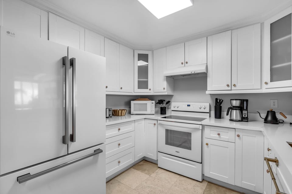 Spacious modern kitchen featuring crisp white cabinetry, full-size refrigerator, and all the essentials for home-cooked meals—stocked, stylish, and ready to make your stay effortless.