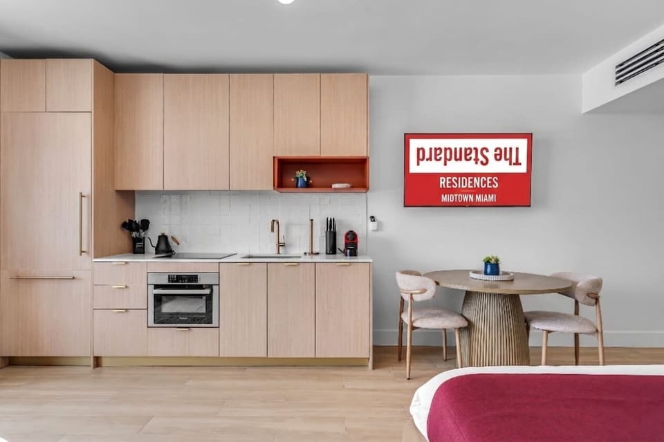 Sleek and modern kitchen featuring light wood cabinetry, built-in appliances, and elegant gold fixtures. Complete with a chic dining nook for two, offering a functional and stylish setup for your urban stay.