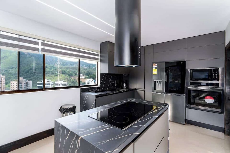 Fully equipped kitchen with a central island, induction stove, oven, microwave, refrigerator, washing machine, and large windows overlooking the city. A modern, comfortable, and functional space to enjoy during your stay.