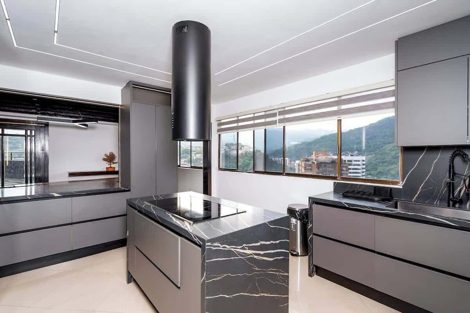 Fully equipped kitchen with a central island, induction stove, oven, microwave, refrigerator, washing machine, and large windows overlooking the city. A modern, comfortable, and functional space to enjoy during your stay.