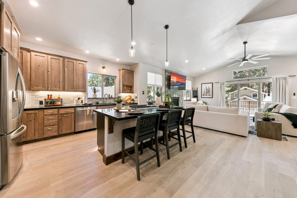 Kitchen island with black granite countertop and woven black stools overlooks the living area with vaulted ceiling and ceiling fan.