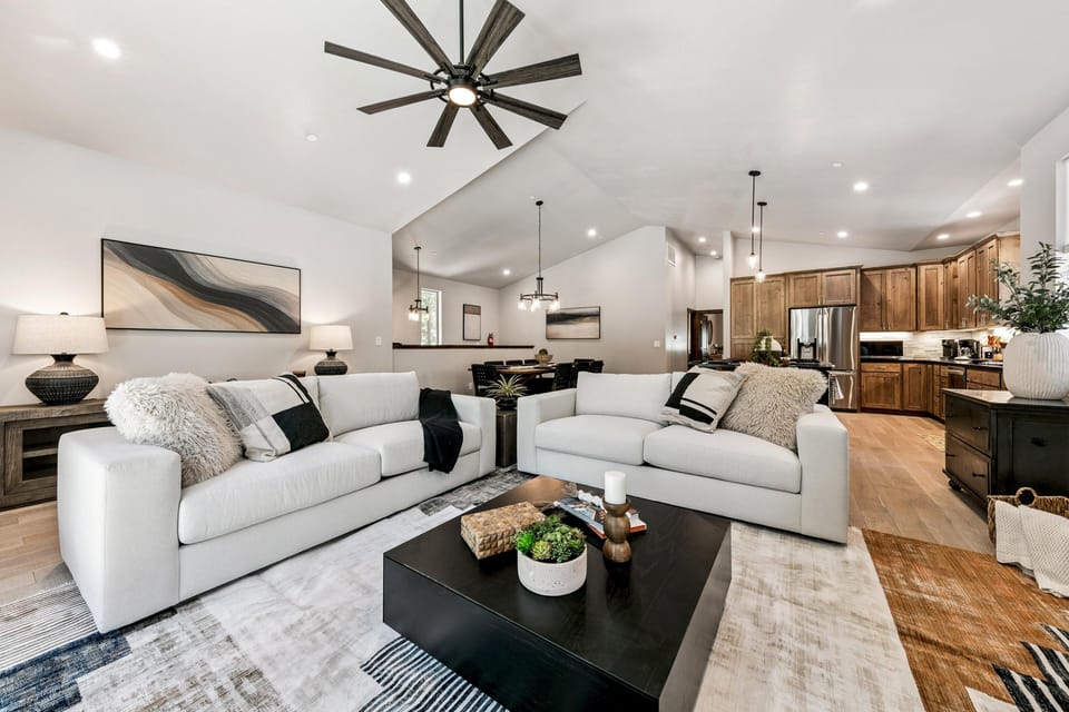 Two light gray sofas face a black square coffee table on a patterned area rug beneath a large ceiling fan.