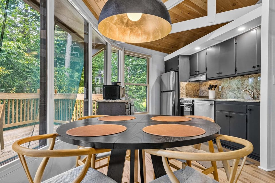 Bright dining nook with treetop views right at the table, steps from a sleek kitchen with stone backsplash.