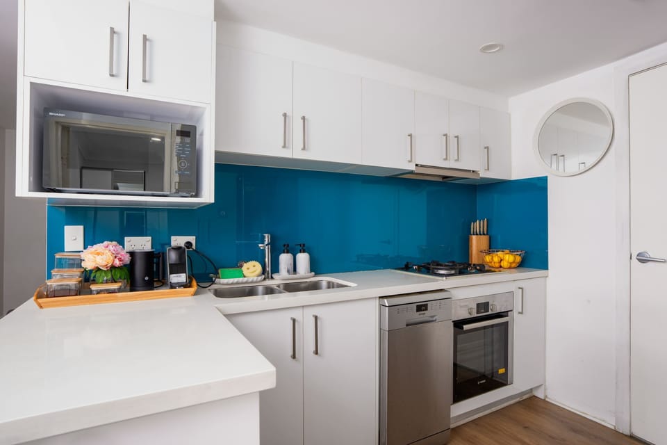 Modern kitchen with white cabinetry, a bright blue splashback, and full-size appliances including an oven, cooktop, and microwave. Well-equipped and bright, with plenty of bench space to cook and prepare meals during your stay. 
