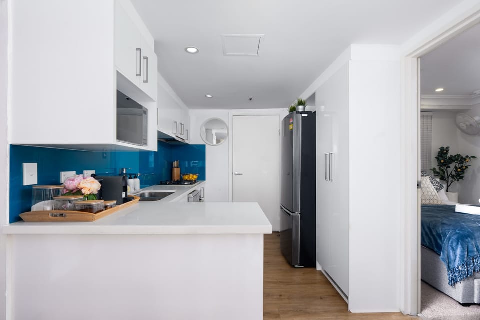 Start your day effortlessly in this 
bright, modern kitchen featuring a sleek blue backsplash, full-sized appliances, and a convenient coffee station just steps away from your cozy bedroom. 

