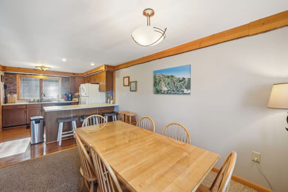 Open living and dining area with warm wood accents, a stone fireplace, and deck access. (Echo)