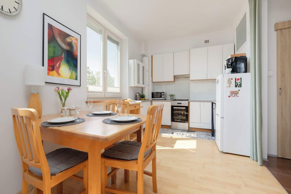 A wooden dining table sits beside the kitchen, creating a comfortable place for meals. Large windows brighten both the dining and cooking areas.