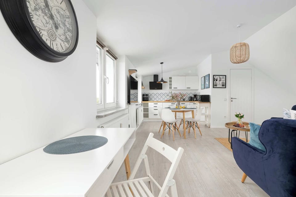 Bright open-plan living area with a dining table, a white desk with a chair, a kitchenette, and a comfortable seating area.