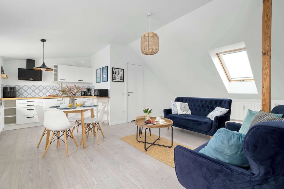 Wide view of the bright living room with blue sofas, dining space, and kitchenette.
