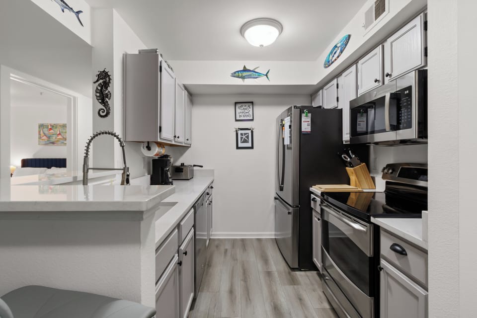 Fully stocked galley kitchen with stainless steel appliances and quartz counters. 