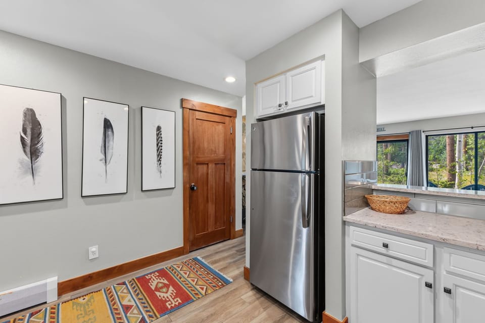 Step into your bright, welcoming space where modern comfort meets mountain charm. Large windows frame a lush forest view, filling the kitchen with natural light as you prepare your morning coffee.