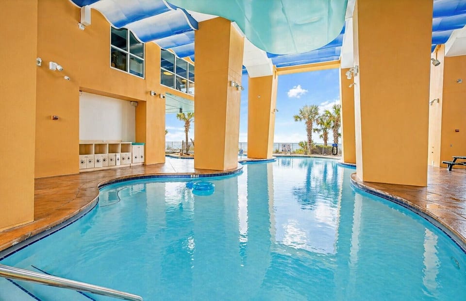 A stunning indoor-outdoor pool with vibrant blue water, palm trees, and ocean views invites relaxation under a retractable canopy.
