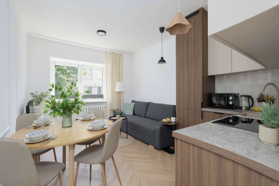 A bright open-plan living space with a dining table, sofa, and modern kitchenette. It's a comfortable place to relax, cook, and enjoy meals together.