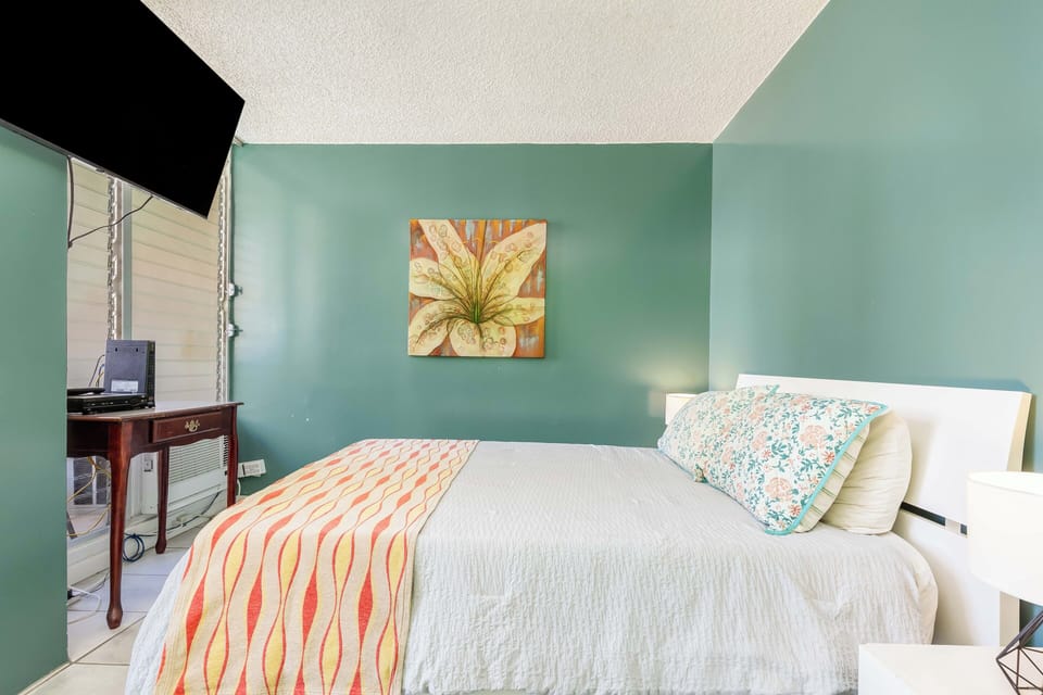 Sink into the plush bed surrounded by soothing turquoise walls, tropical artwork, and bright natural light streaming through your private outdoor access.